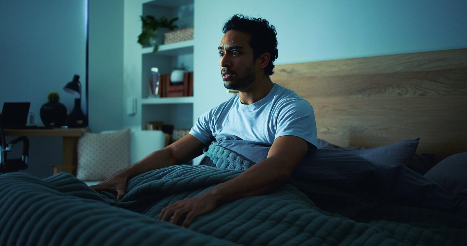 Insomnia, scared and man in bedroom at night for burnout, exhausted and fatigue for mental health. Tired, dark and person with fear, awake and afraid for sleepless, bad dream and nightmare in home